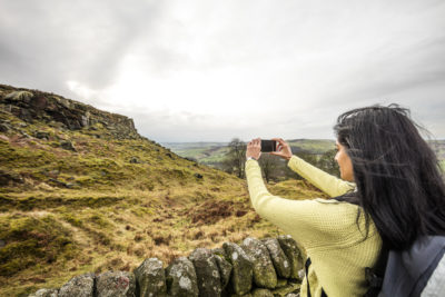 The landscape of the Peak District National Park, Derbyshire, woman taking a picture with her smartphone.