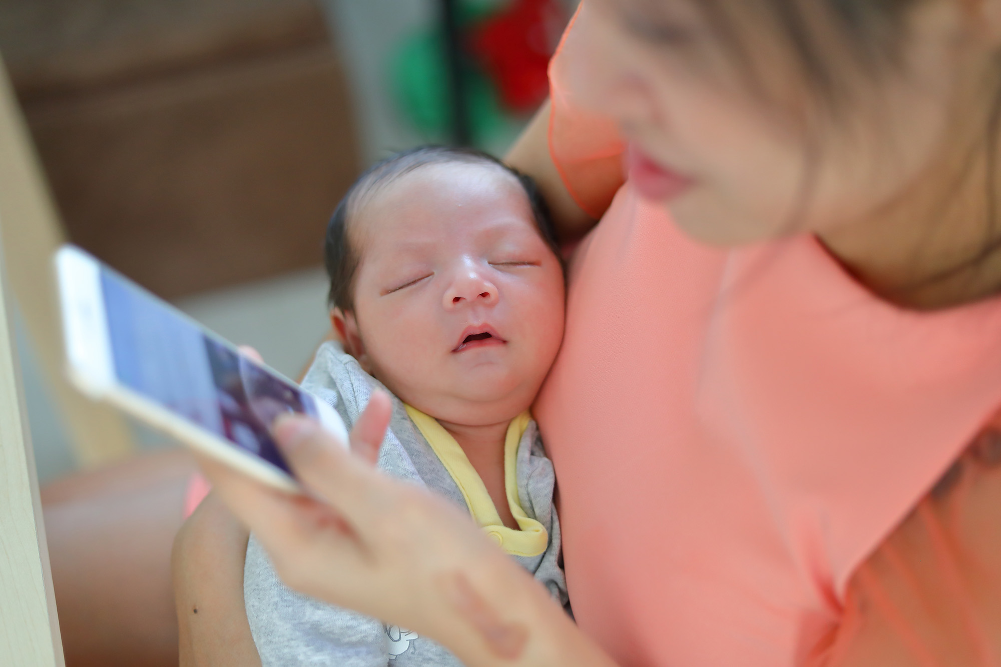 mother playing mobile phone in business home office with cute baby newborn sleeping