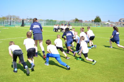 A bunch of children are doing lunges outside on an astroturf