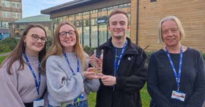 A picture of Shannon smiling for the camera, with two other students and a teacher, outside of a college